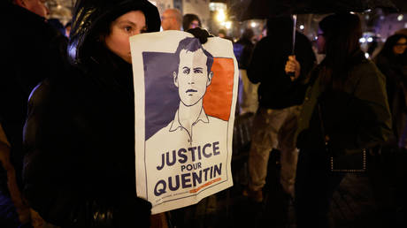 A woman holds a placard reading "Justice for Quentin" as she pays tribute to Quentin Deranque, 23, who died in Lyon from a street beating, Lille, France, February 18, 2026.
