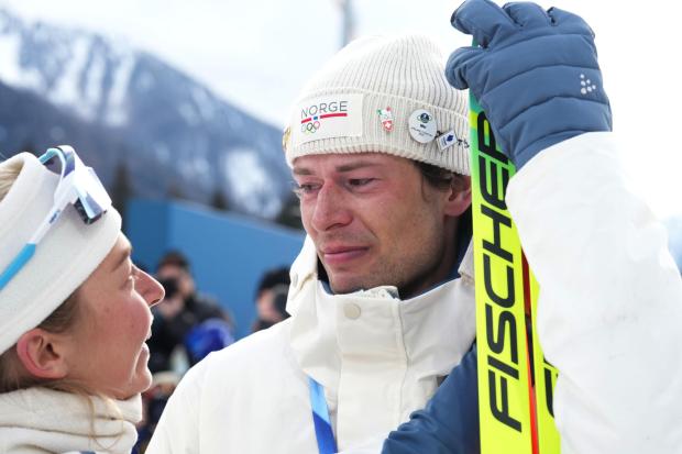 Sturla Holm Laegreid, of Norway, reacts after he won bronze as teammate Ingrid Landmark Tandrevold comforts him after the men's 20-kilometer individual biathlon race at the 2026 Winter Olympics