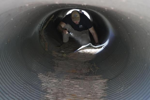 An investigator looks inside a culvert in the neighborhood where Annie Guthrie, whose mother Nancy Guthrie has been missing for more than a week, lives just outside Tucson, Ariz., on Tuesday, Feb. 10, 2026. (AP Photo/Ty ONeil)