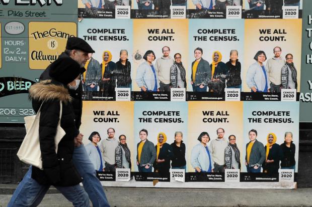 FILE - People walk past posters encouraging participation in the 2020 Census in Seattle's Capitol Hill neighborhood, April 1, 2020. (AP Photo/Ted S. Warren, File)