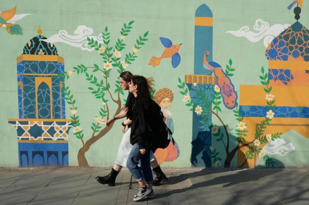 Women walk past an Islamic-themed painting on a wall