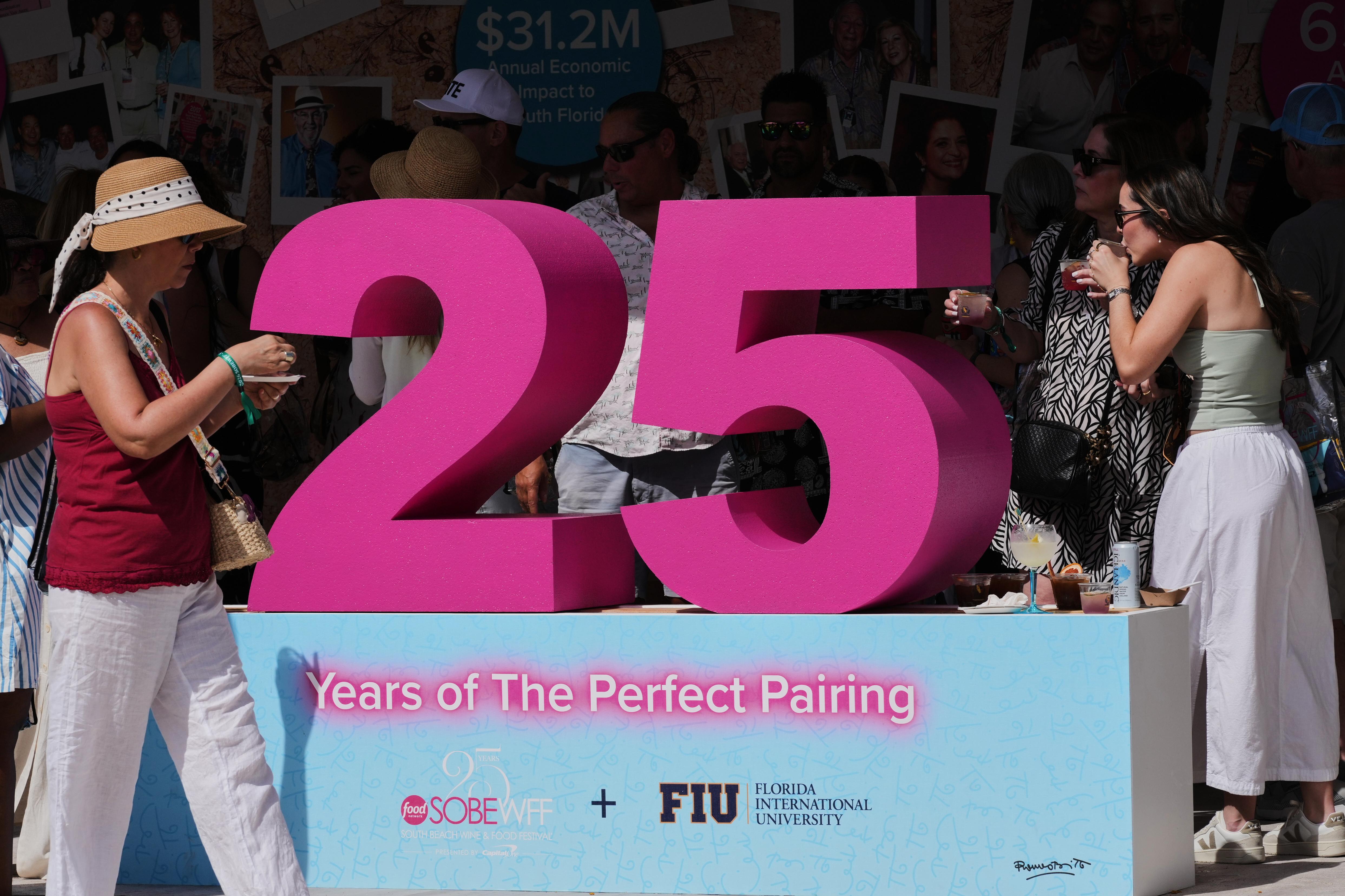 Attendees walk by the Florida International University 25th anniversary tent...