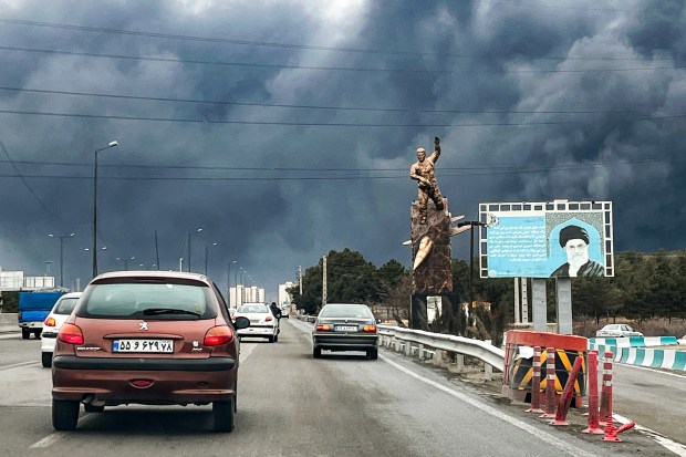 Vehicles move along a highway past a war memorial statue and a billboard depicting Iran's late supreme leader Ayatollah Ali Khamenei who was killed in an air strike on February 28, with plumes of black smoke billowing, in Tehran on Sunday. (Photo by AFP via Getty Images)