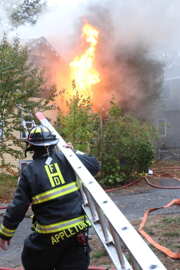 A firefighter carries a ladder during efforts to douse a 2-alarm blaze on Essex Avenue in Hamilton Sunday, October 12, 2025. (Photo by Glenn Preston, Boston Herald)