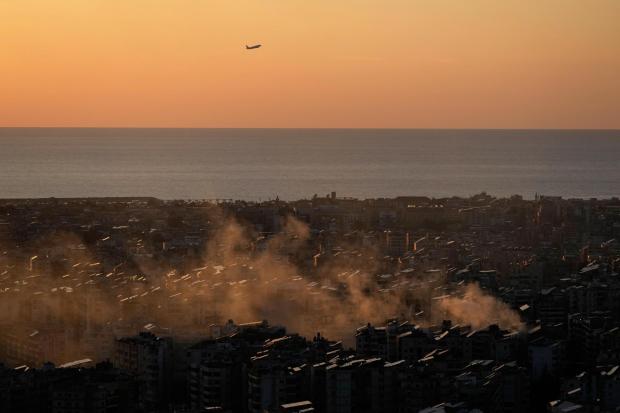 A plane takes off from the Beirut-Rafic Hariri International Airport as smoke from an airstrike rises.