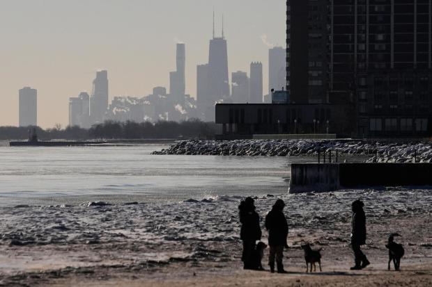 People walk their dogs on an ice covered beach at the Lake Michigan shore, Tuesday, Jan. 20, 2026, in Chicago. (AP Photo/Kiichiro Sato)