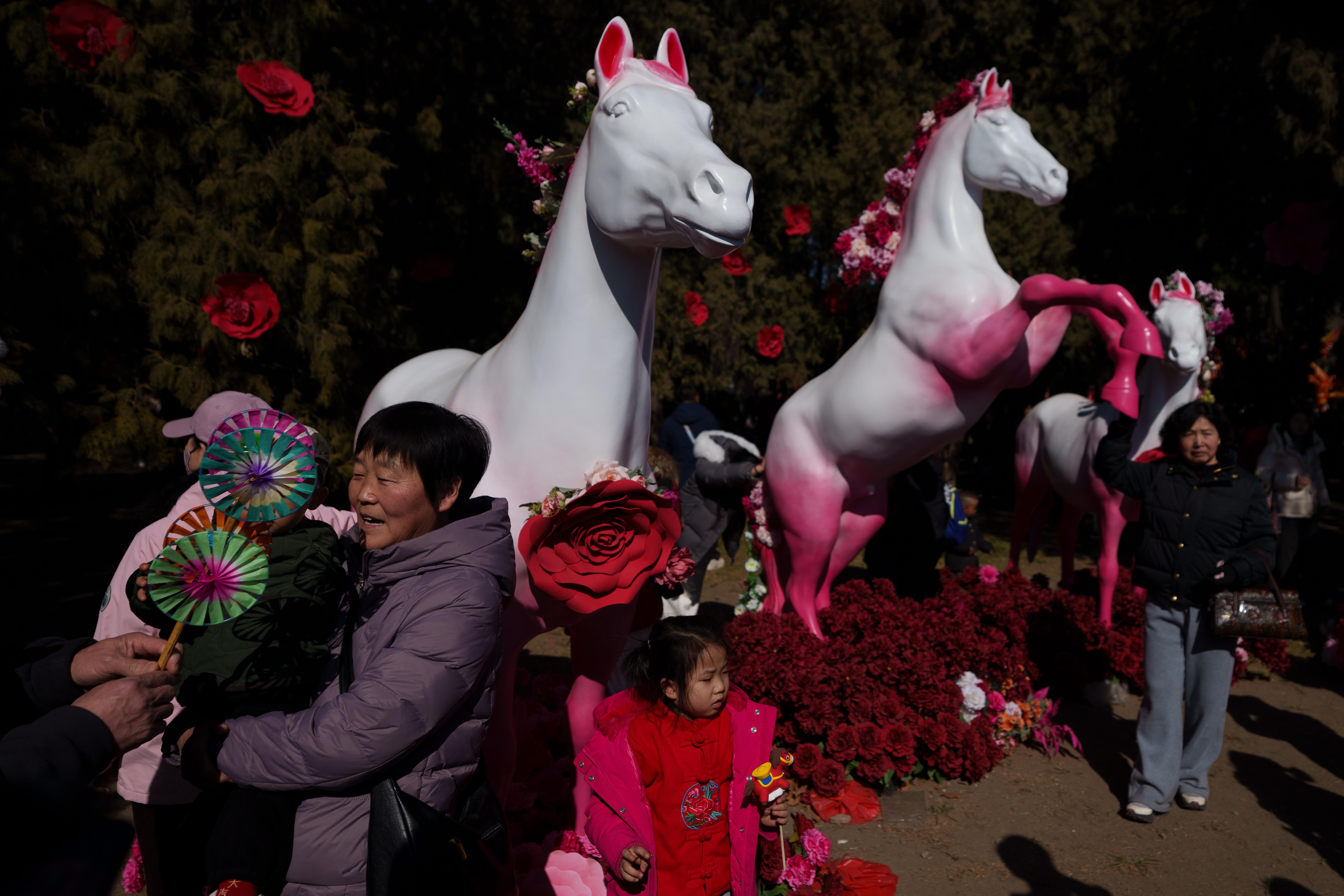 Visitors pose beside decorative horse sculptures at a temple fair...
