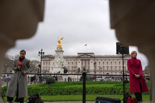 Reporters stand in front of Buckingham Palace.