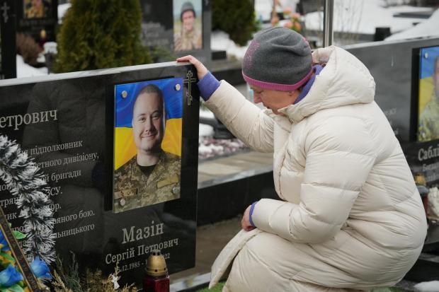 A woman sits in front of a relative's grave during a memorial service for fallen Ukrainian soldiers.