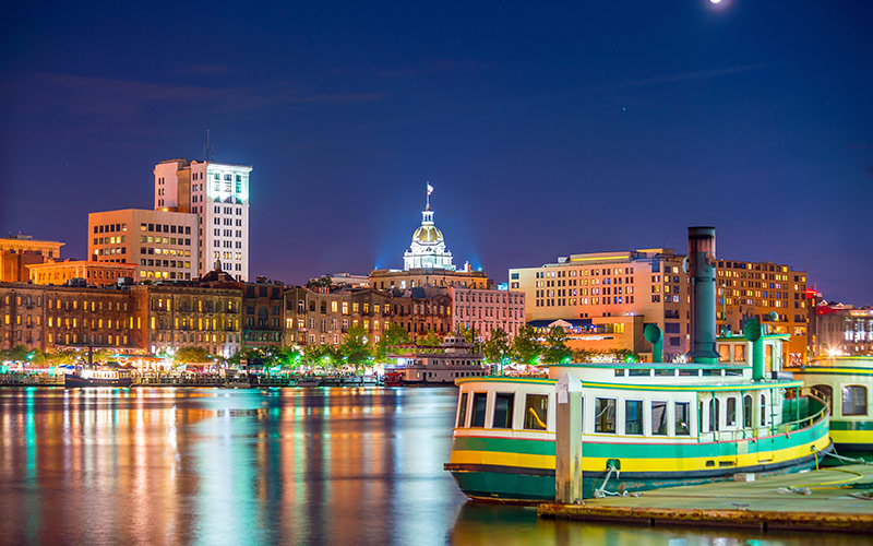 Scenic waterfront of Savannah, Georgia, with historic buildings and boats along the river