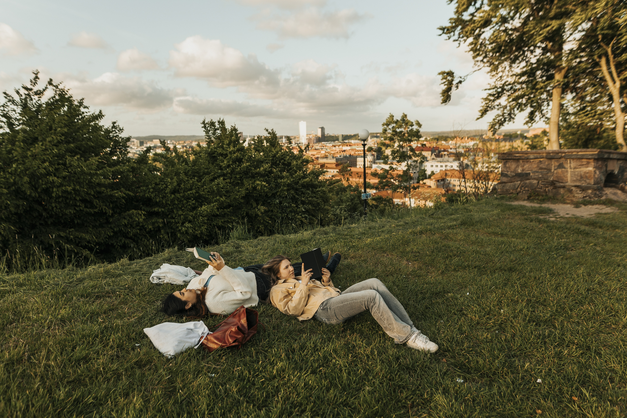 Female friends reading book while lying down on grass at a hill.