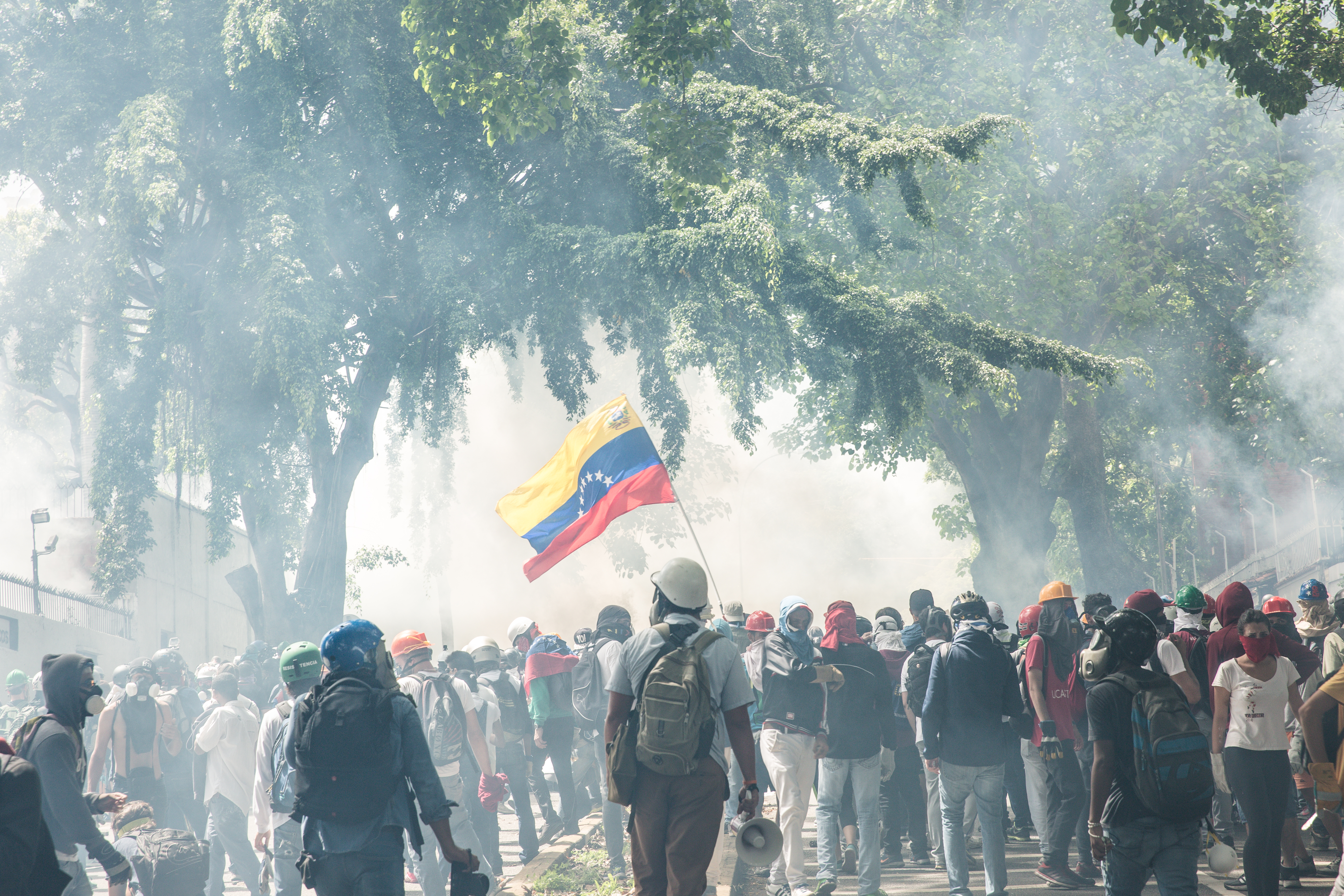 A group of protesters hold a Venezuelan flag as the air is thick with tear gas. 