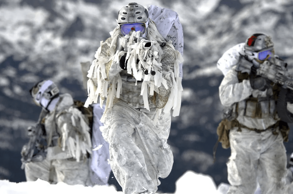 Soldiers in white camouflage in snowy terrain.