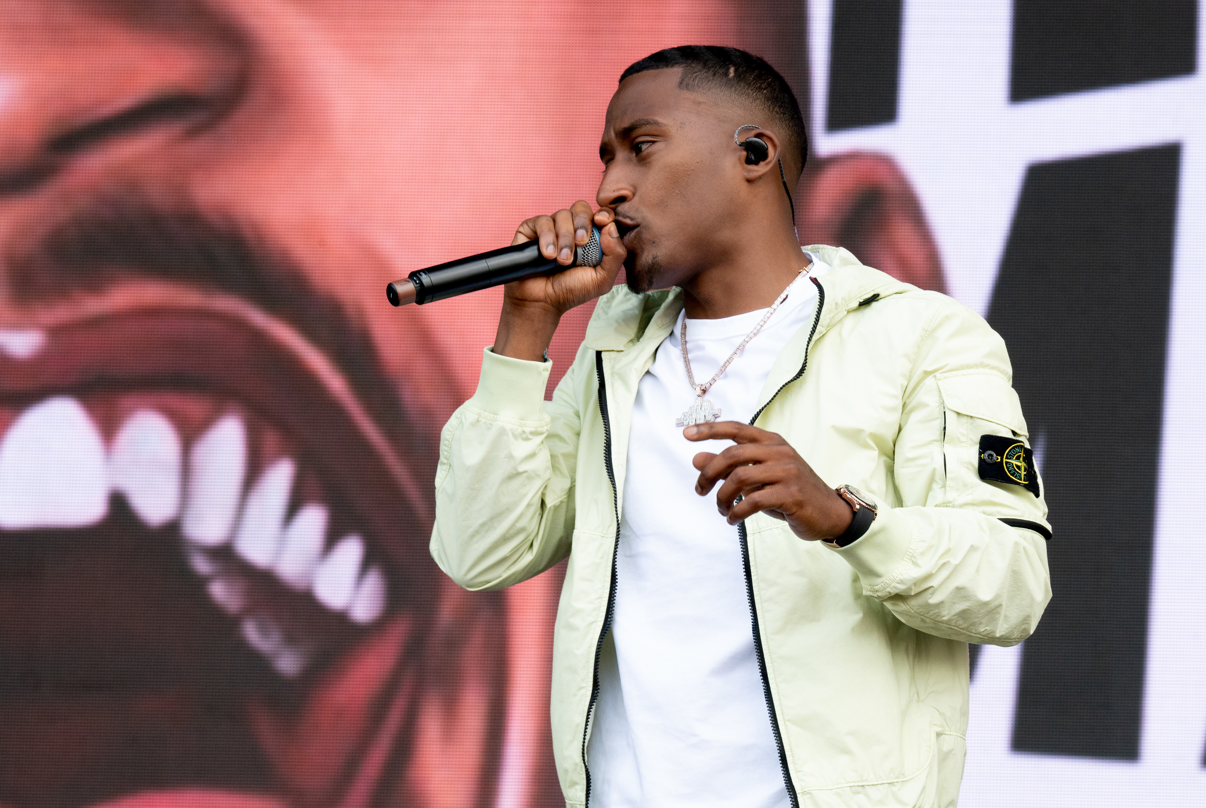 a man wearing a stone island jacket sings into a microphone