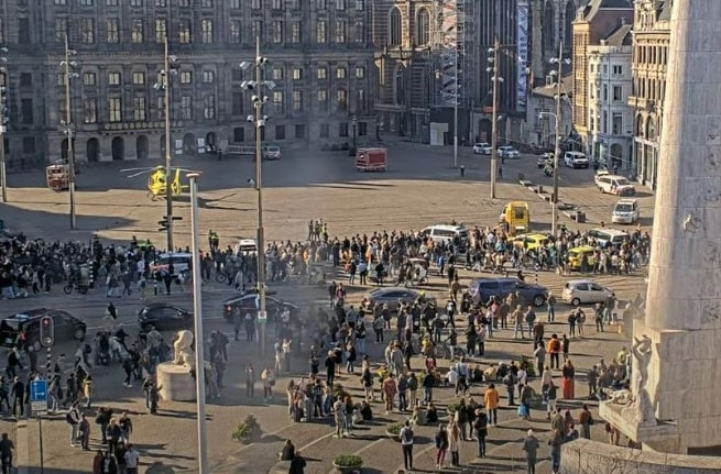 Aerial view of a large crowd gathered in a city square, with emergency vehicles and a helicopter present.