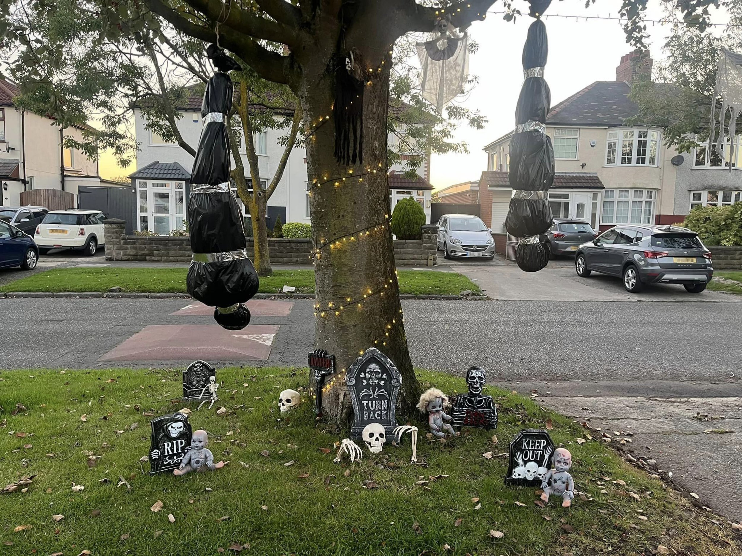 PIC FROM Kennedy News/Caroline Ashley - not rights cleared, used in public interest (PICTURED: THE BODY BAG HALLOWEEN DECORATIONS SWINGING FROM A TREE ON COUNCIL-OWNED LAND IN FRONT OF CAROLINE ASHLEY'S HOUSE) A mum claims she was forced to tear down her body bag Halloween decorations by the council after killjoy 'Karen' neighbours complained about the life-sized props swinging from a tree. Caroline Ashley, from Liverpool, Merseyside, was stunned when a Liverpool Council worker allegedly rang her doorbell on September 24th demanding she remove the offending decorations from a tree in front of her house. The 41-year-old says the council visit followed a 'really upset' local who banged on her door to say she was 'triggered' by the display. DISCLAIMER: While Kennedy News and Media uses its best endeavours to establish the copyright and authenticity of all pictures supplied, it accepts no liability for any damage, loss or legal action caused by the use of images supplied and the publication of images is solely at your discretion. SEE KENNEDY NEWS COPY - 0161 697 4266