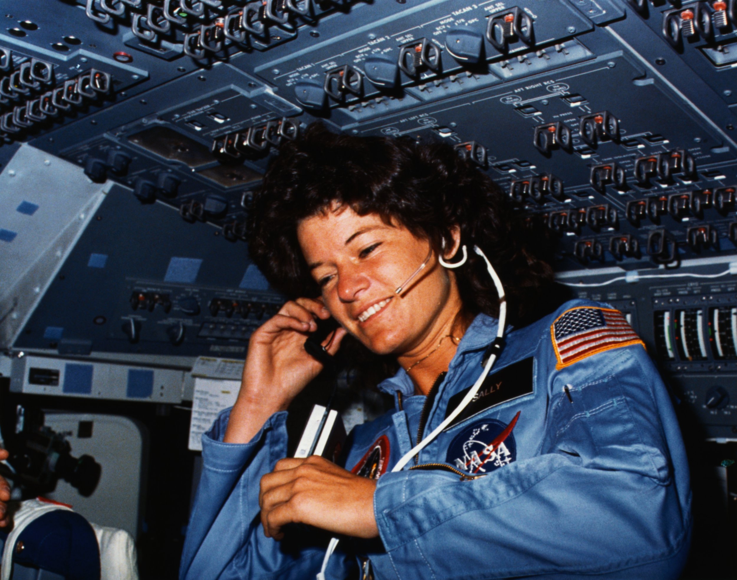 (Original Caption) Johnson Space Center, Houston, Texas: On board Scene-Astronaut Sally K. Ride, STS-7 mission specialist, communicates with ground controllers from the flight deck of the Earth-orbiting Space Shuttle Challenger. Dr. Ride holds a tape recorder. The photograph was taken by one of her four fellow crewmembers with a 35mm camera.